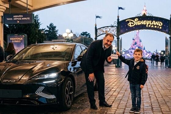 Driver holding a name sign beside a child at the illuminated Disneyland Paris entrance